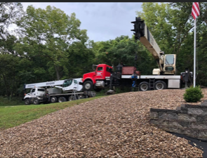 Two crane trucks on a hillside, one red, one white, reaching over gravel and grass.
