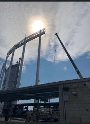 Crane near stadium lights in bright sunlight. Blue sky.