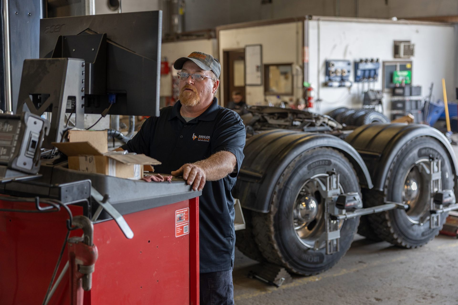 Man in a garage working on a truck's wheels. He's using a machine with a monitor. The setting is an auto repair shop.