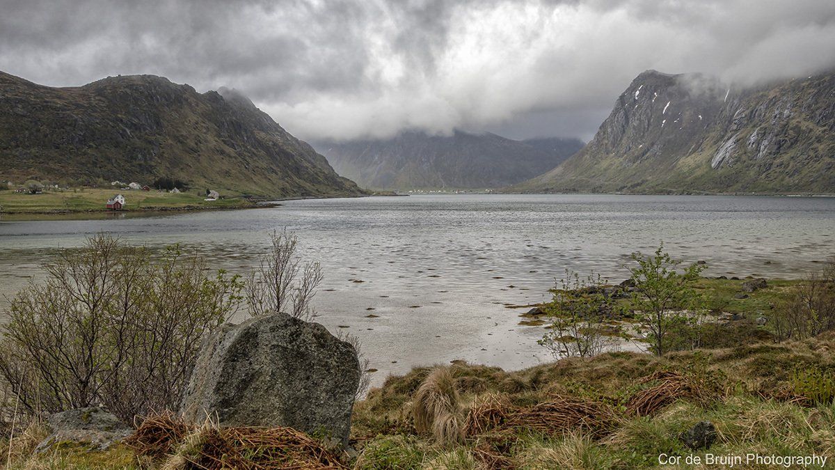 A lake between mountains under a cloudy sky. Rain falls on the water and the surrounding terrain.