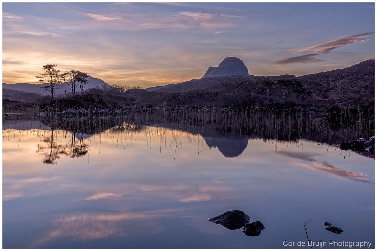 Mountain reflected in a calm lake at sunrise, with pink and blue sky.