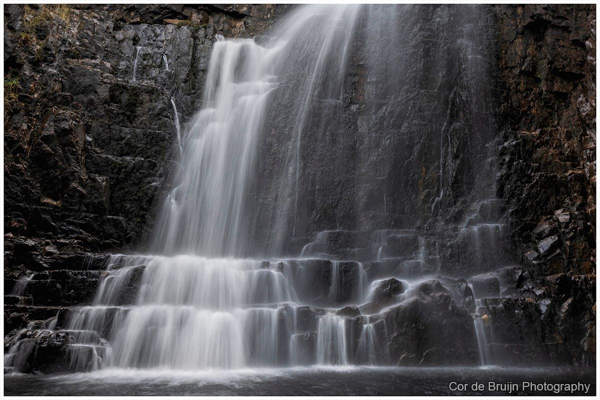 Waterfall cascading over dark rock ledges in a wooded setting
