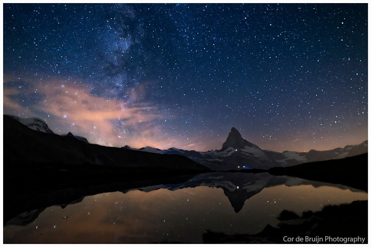 Night sky over mountain, stars reflecting in lake.