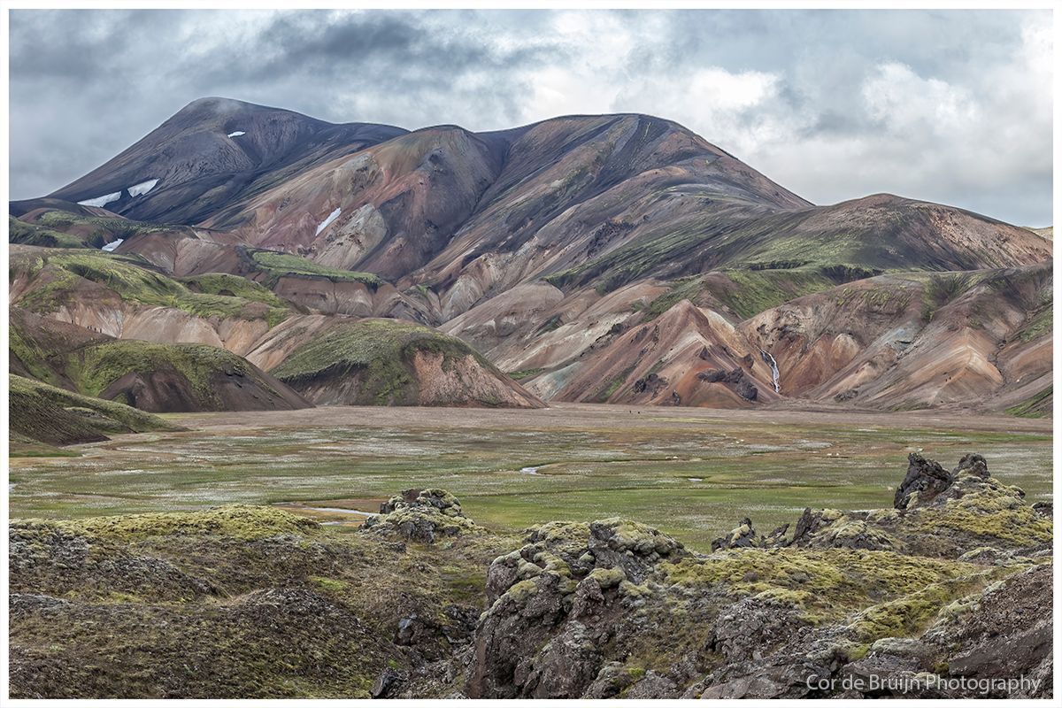 Colorful mountains and valley under a cloudy sky. Green moss in the foreground.