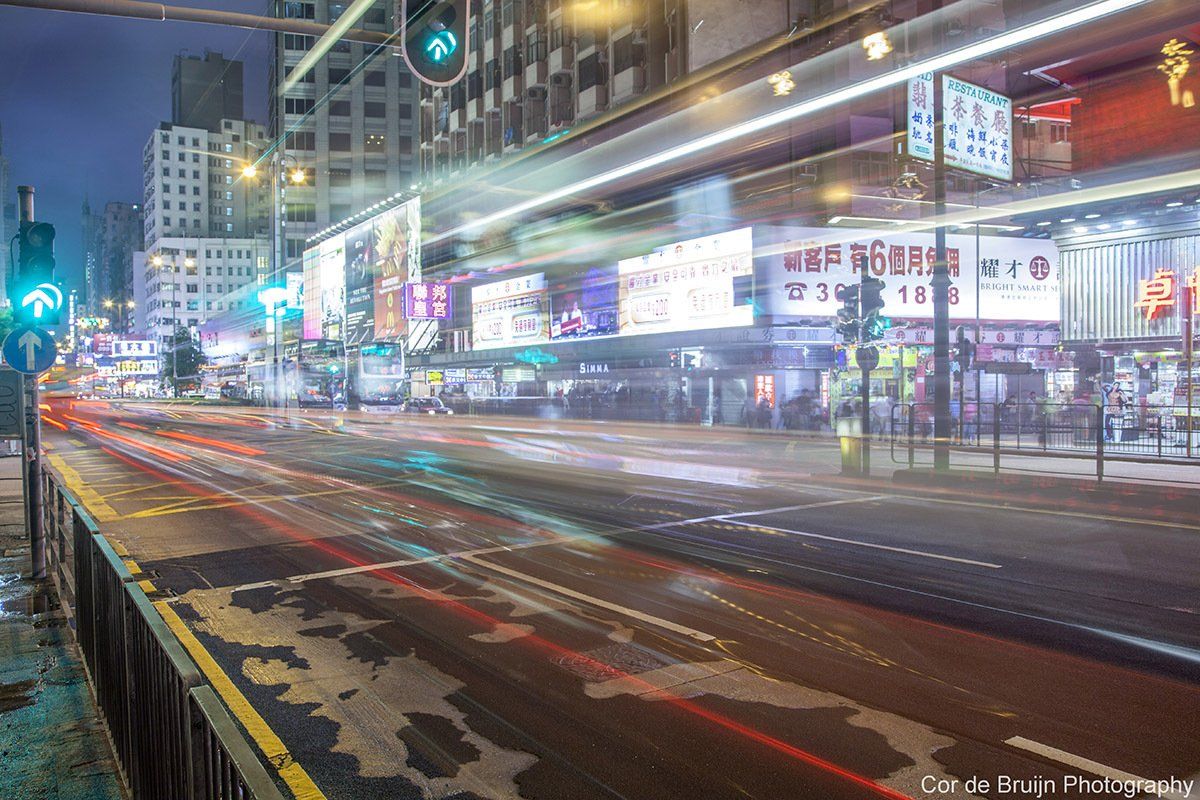 Night cityscape with blurred streaks of car lights; green traffic lights, neon signs, and commercial buildings.
