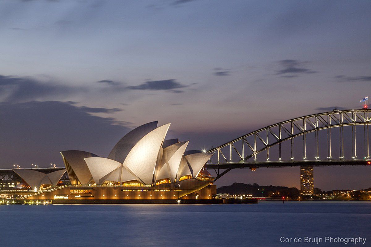 Sydney Opera House and Harbour Bridge at dusk, illuminated against a dark blue sky.