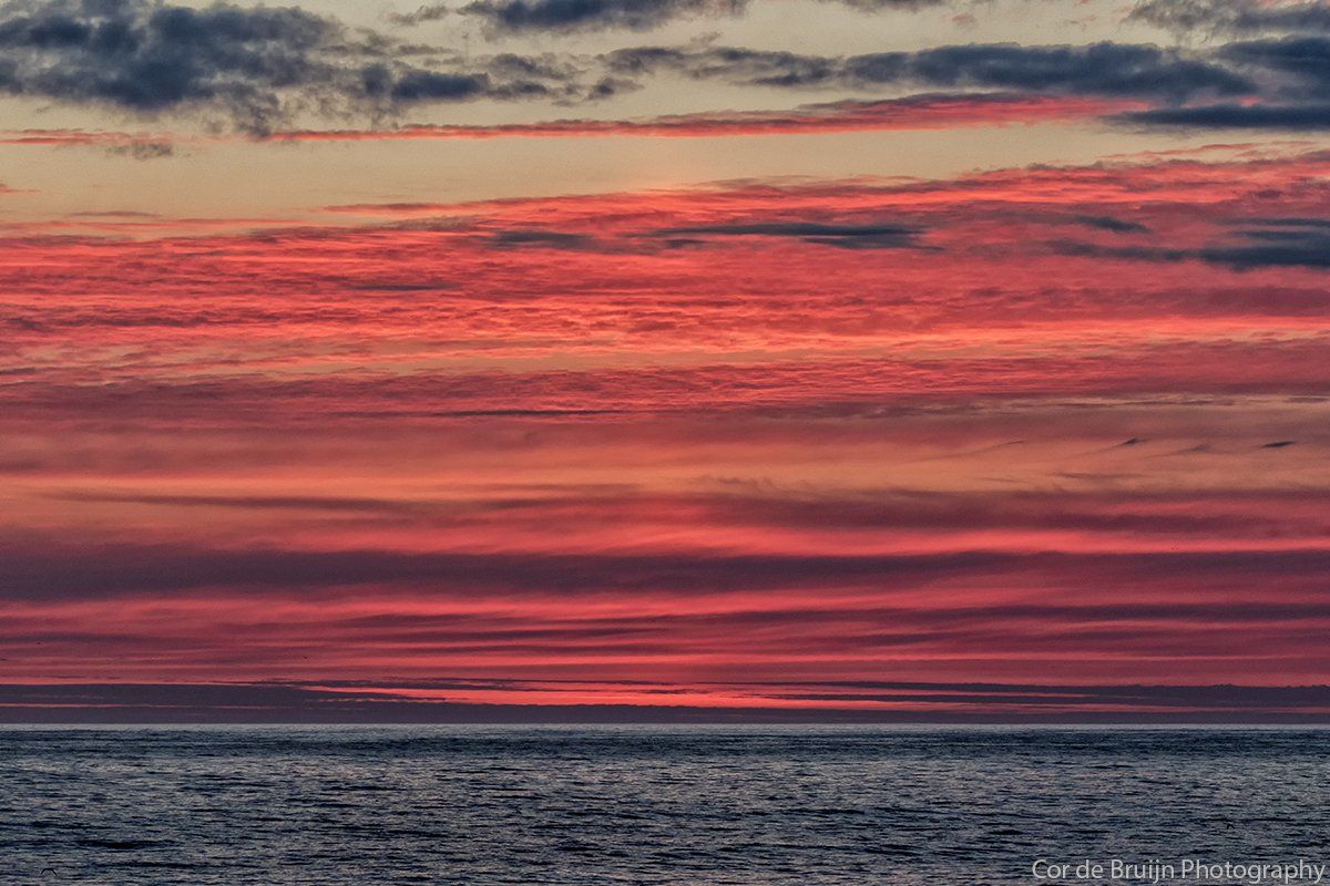 Crimson and orange sunset over a calm ocean with dark gray clouds.