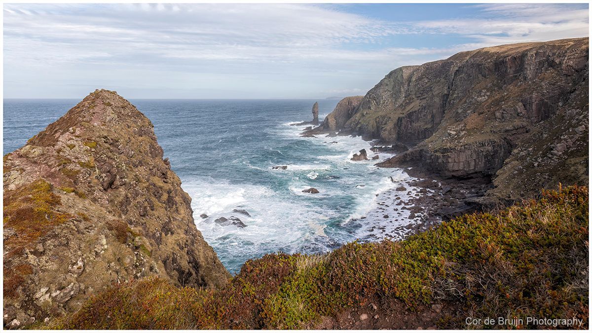 Rocky coastal cliffs overlooking a choppy blue ocean under a pale cloudy sky