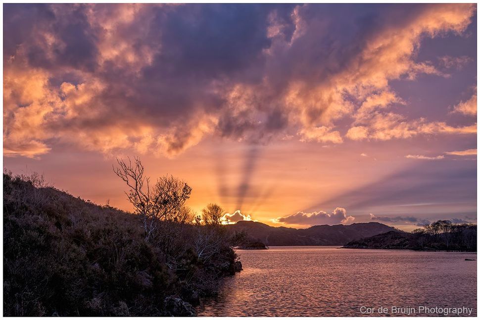 Sunset over a calm lake with dramatic pink clouds and silhouetted trees and hills