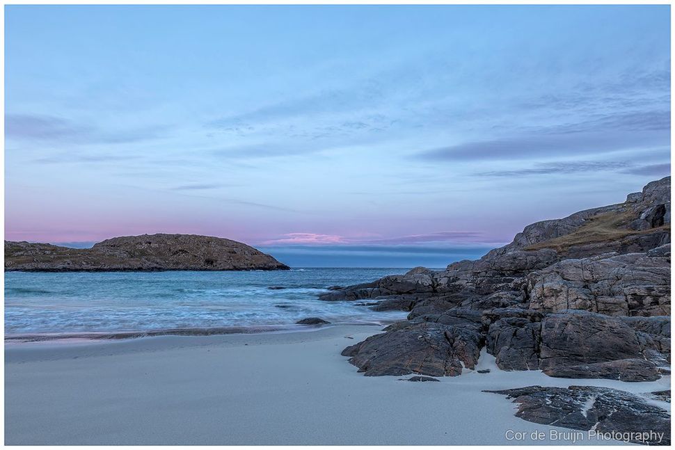 Calm beach at dusk with blue sky, gentle waves, and rocky outcrops on both sides