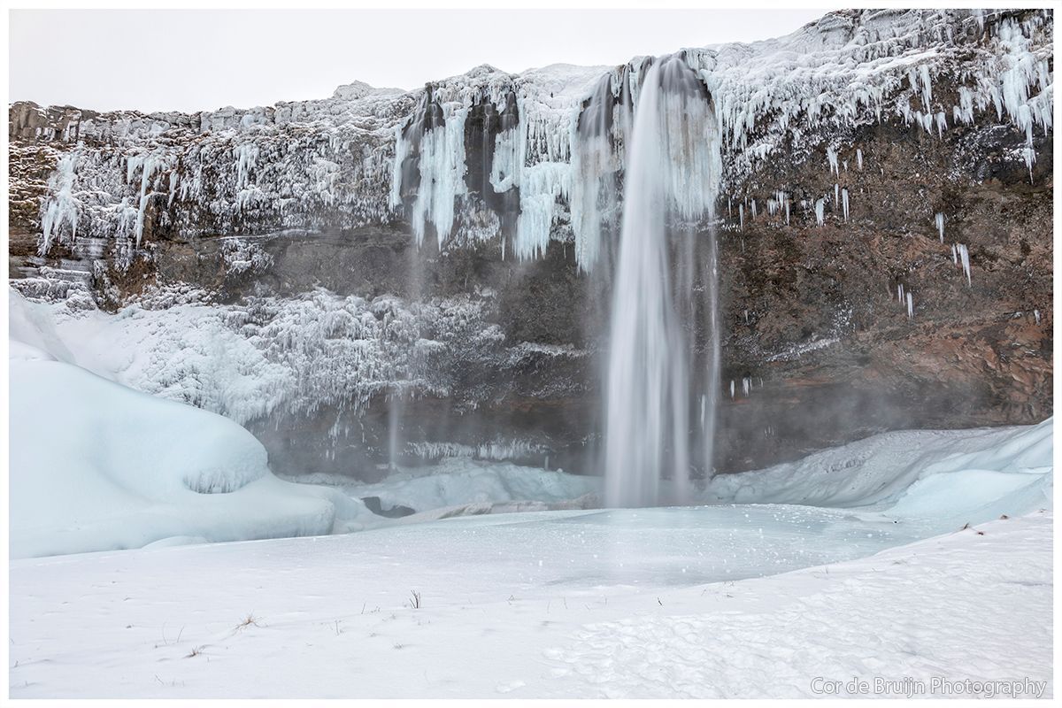 Waterfall cascading down a cliff, surrounded by ice and snow in a winter landscape.
