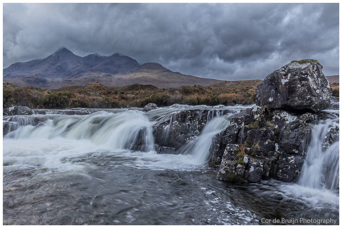 Water cascading over rocks; mountain in background under a stormy sky.