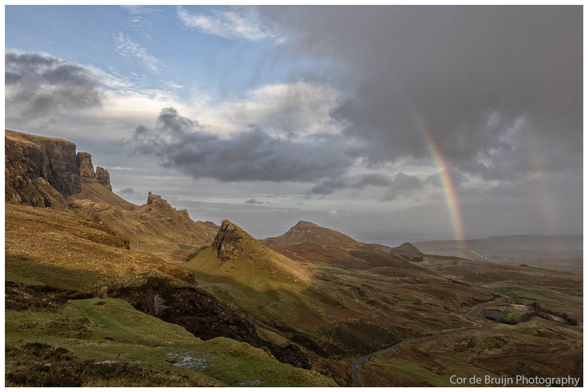 Mountain landscape with a rainbow, dramatic sky, and sunlit ridges.