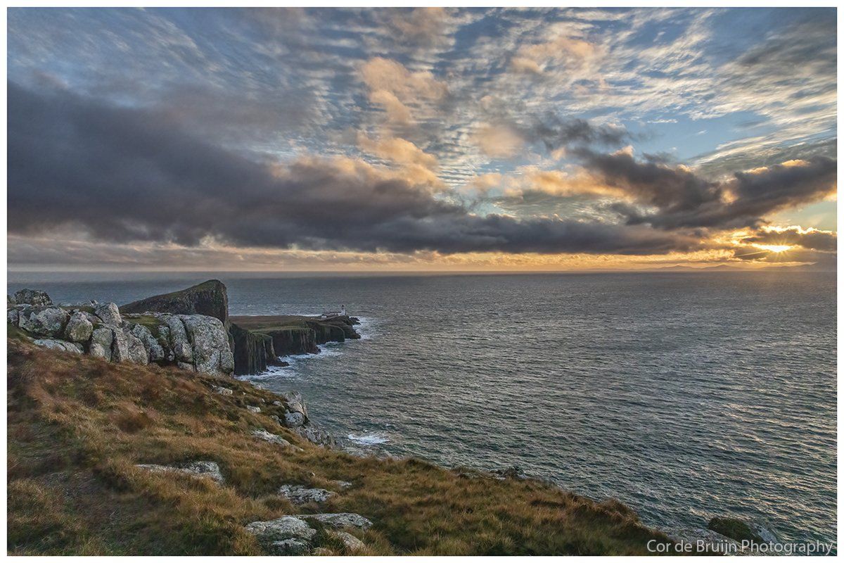 Rocky coastline under a cloudy sky at sunset. The sea is choppy with golden light breaking through the clouds.