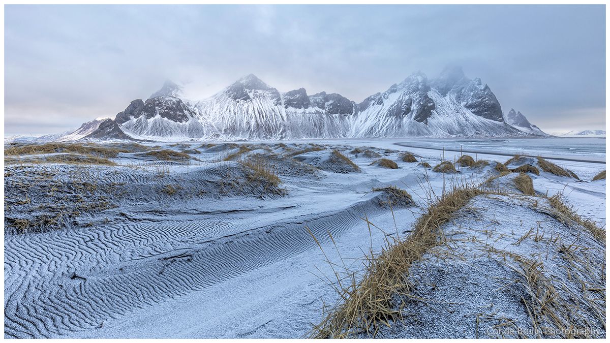 Snow-covered mountains and dunes under a cloudy sky.