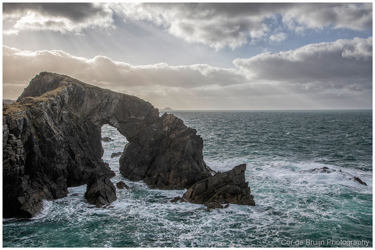 Rock arch in ocean with choppy water and cloudy sky.
