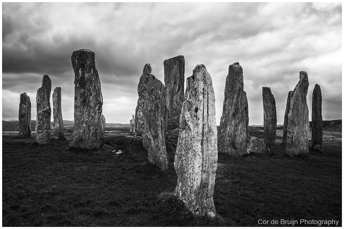 Black and white photo of standing stones in a field under a cloudy sky.