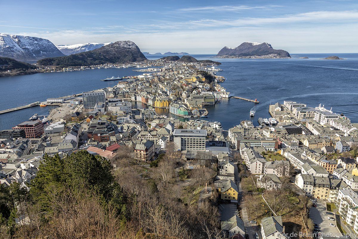 Aerial view of Ålesund, Norway, a coastal city with colorful buildings, mountains, and sea on a sunny day.