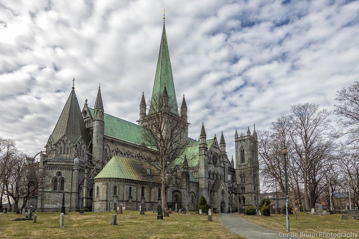 Nidaros Cathedral, Trondheim, Norway, a Gothic stone church with a tall spire and green roof, under a cloudy sky.
