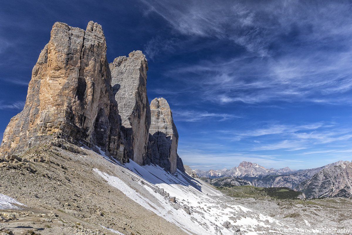 Three jagged mountain peaks with snow patches under a bright blue sky.