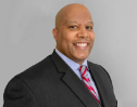 Smiling man in a suit and tie, positioned against a gray backdrop.