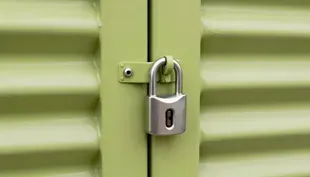 Green storage unit hallway with rows of metal doors and bright overhead lights