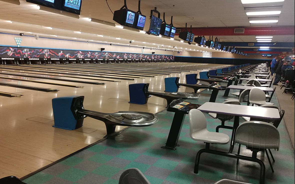 Green bowling ball in the foreground with white pins lined up behind it on a glossy lane.