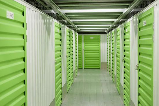 Green storage unit hallway with rows of metal doors and bright overhead lights