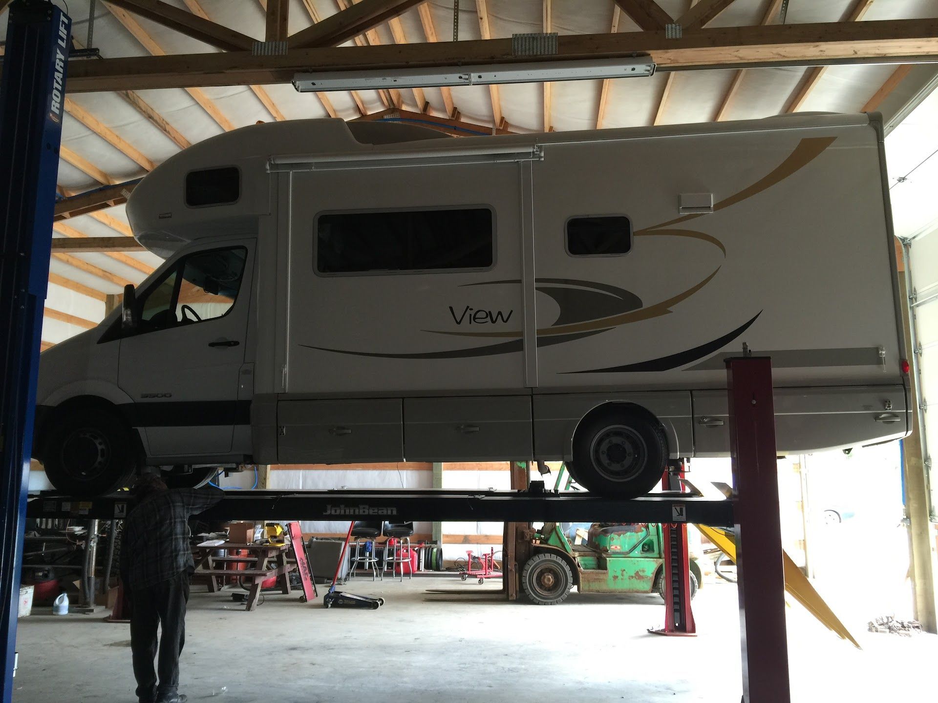 RV on a lift in a repair shop. White vehicle with brown trim, seen from the side. Inside a garage | South Beach Towing & Repair