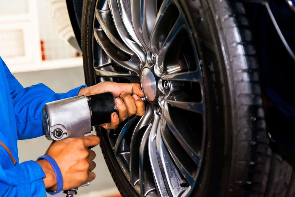 A Man Uses an Air Wrench to Change a Tire on A Car — Torque Tyres & Trailer Spares Cairns in Cairns, QLD