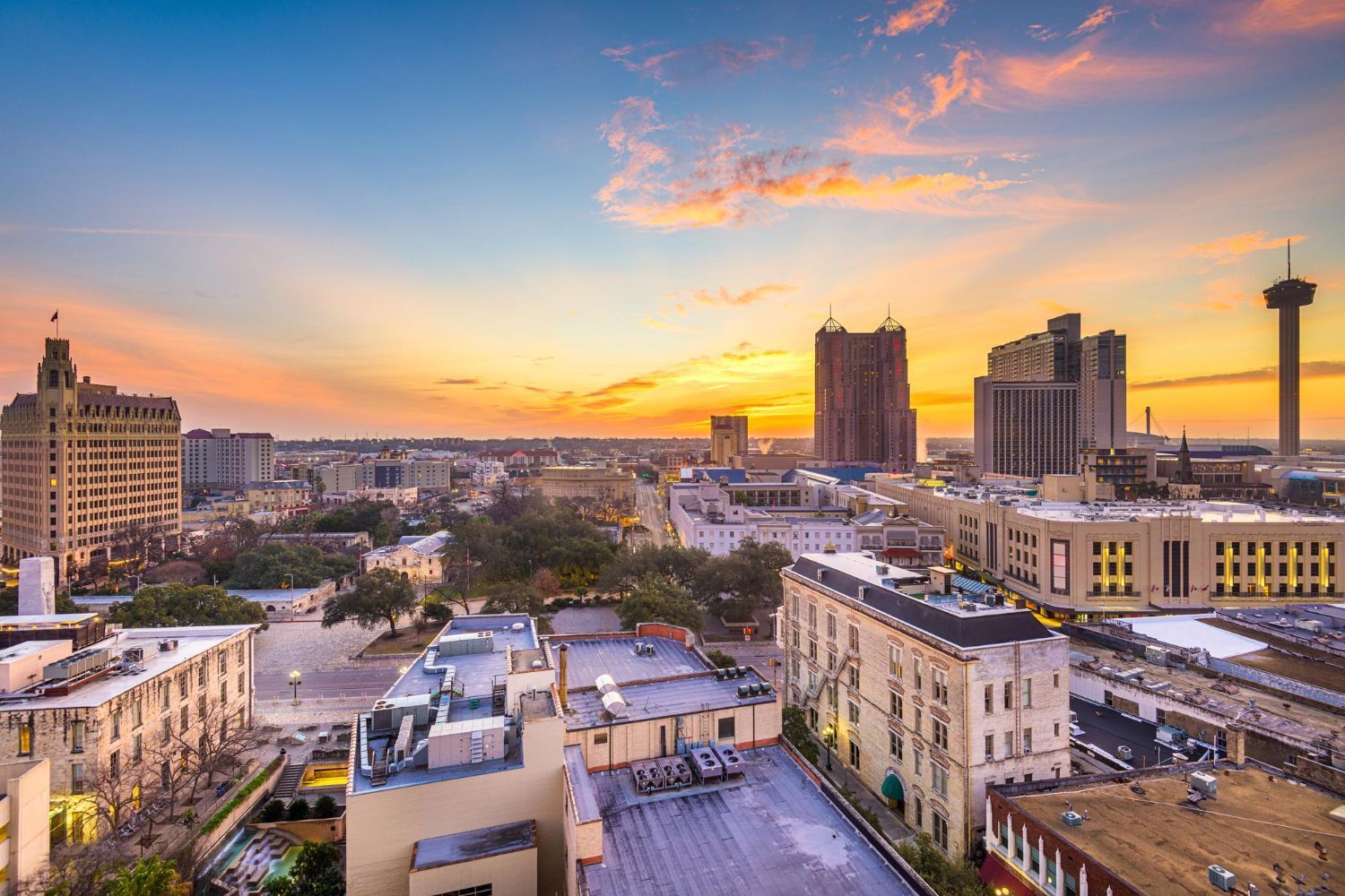 Sunset over a city skyline with high-rise buildings and a tall tower under pink-orange clouds