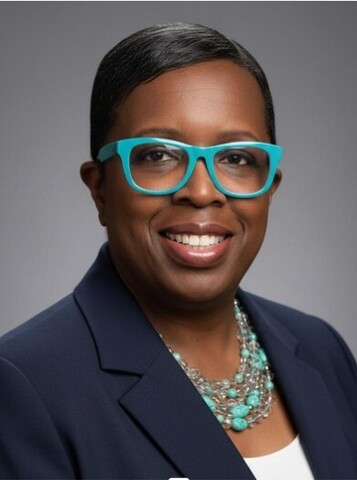 Portrait of Tina Nelson in a navy blazer and turquoise glasses, wearing a matching necklace.