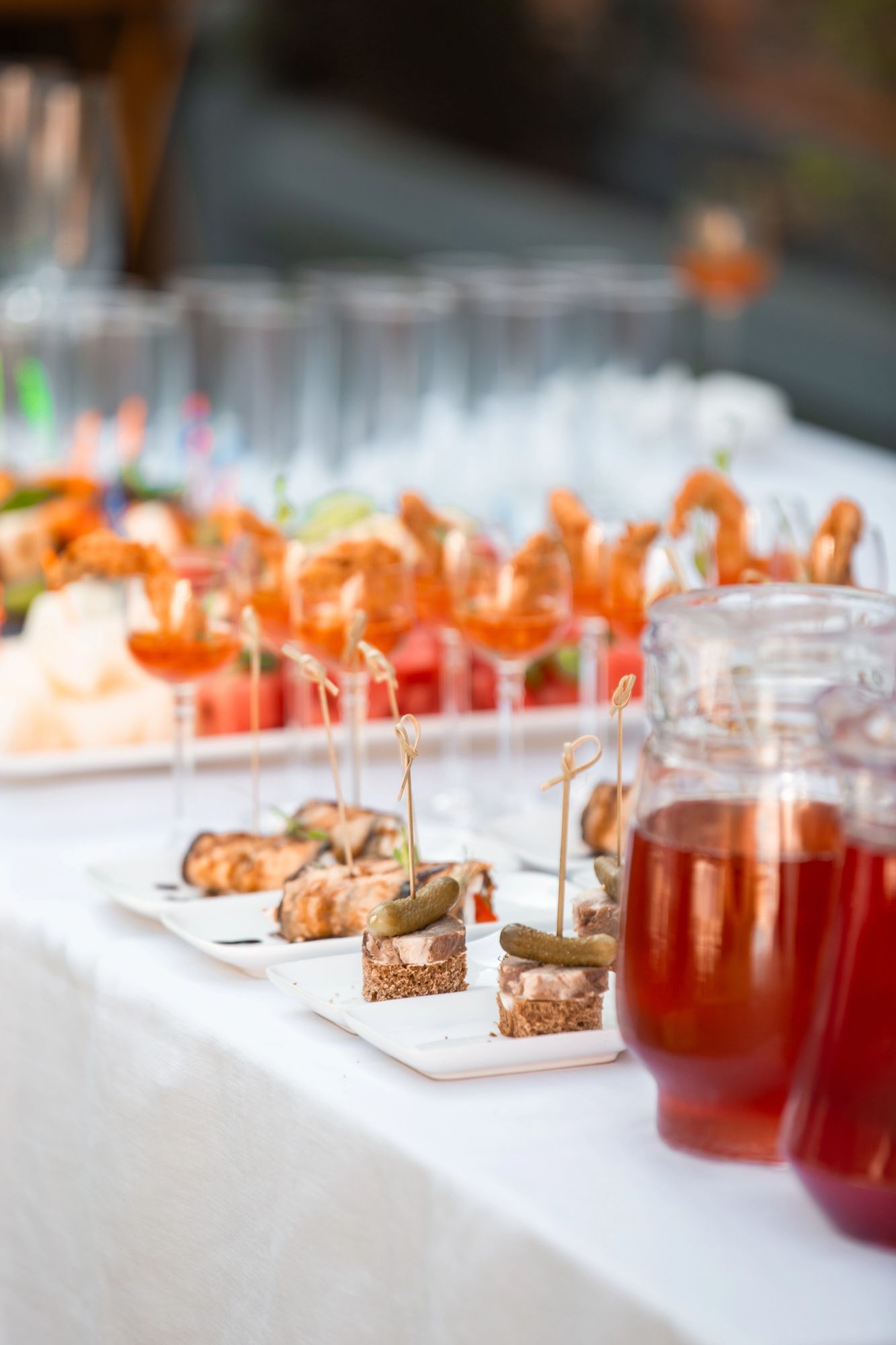 Un tavolo apparecchiato per un buffet con antipasti di gamberi in bicchieri, tartine con sottaceti e caraffe di succo rosso.