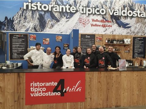 Un gruppo di dipendenti di un ristorante in uniforme si trova dietro un bancone di legno, di fronte a uno sfondo a tema montano.