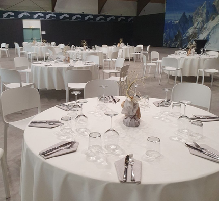 Una sala per banchetti piena di tavoli rotondi coperti da tovaglie bianche, apparecchiati con posate e sedie bianche.