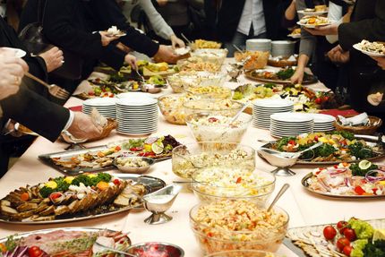 In un evento con servizio di catering, le persone si servono da sole da un lungo e affollato tavolo a buffet, attingendo a una vasta gamma di cibi.