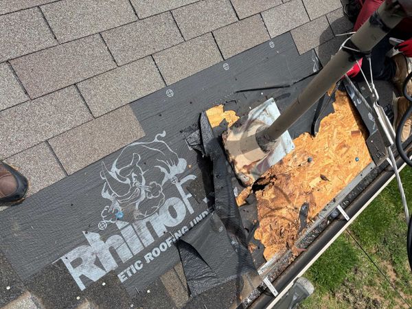 Damaged rooftop with torn black roofing under a fallen pole, showing exposed yellow insulation and a grassy edge