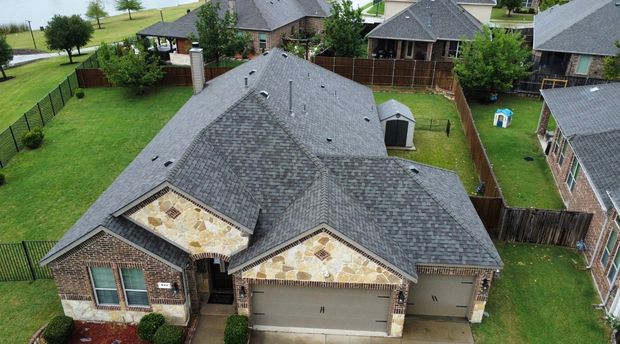 Aerial view of a suburban house with a gray roof, attached garage, and fenced backyard on a rainy day