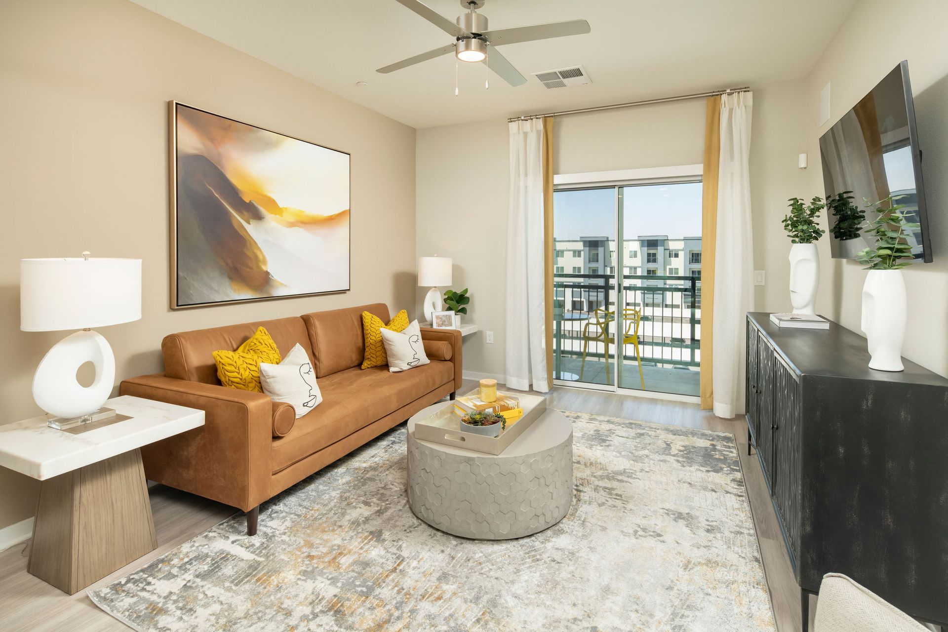 Living room in a modern apartment with a tan sofa, rug, and sliding balcony door.
