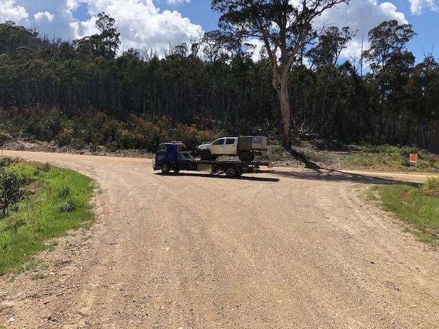 A tow truck is towing a white ute on a dirt road — Crossborder Towing in Thurgoona, NSW