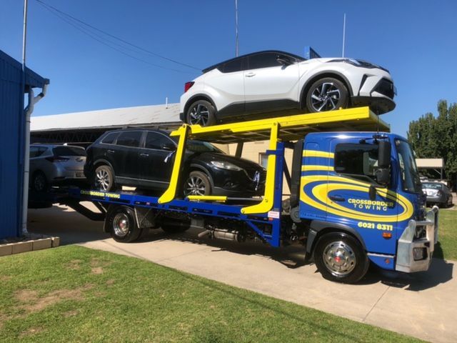A blue tow truck is carrying two cars— Crossborder Towing in Howlong, NSW