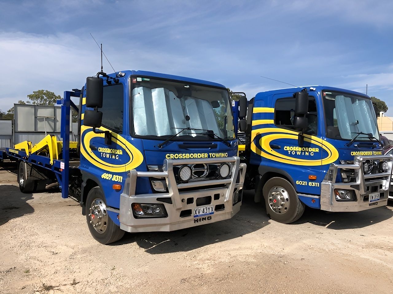 Two Blue and Yellow Trucks Are Parked Next to Each Other on a Dirt Road — Crossborder Towing in Lavington, NSW
