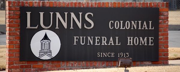 Lunns Colonial Funeral Home sign on a brick wall, with black and white lettering.