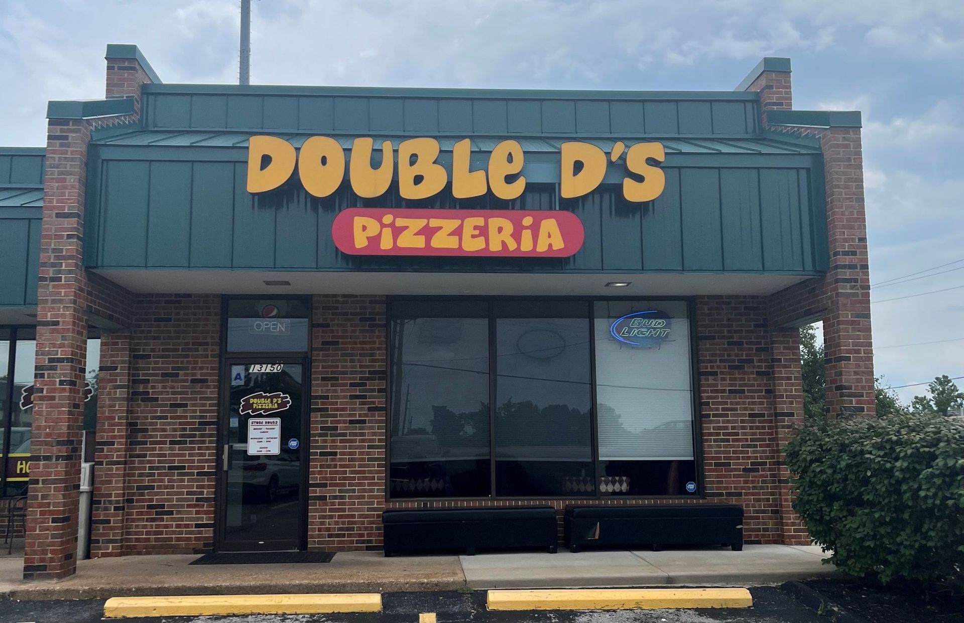 Double D’s Pizzeria storefront with brick facade and blue awning, seen from the parking lot