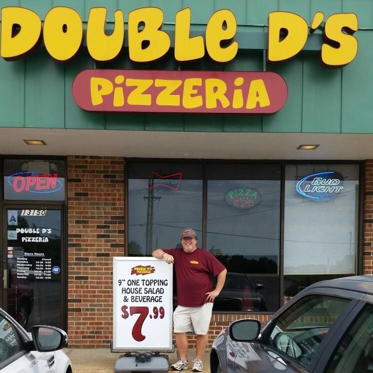 Man standing outside Double D’s Pizzeria holding a sign advertising $7.99 dine-in and takeout special