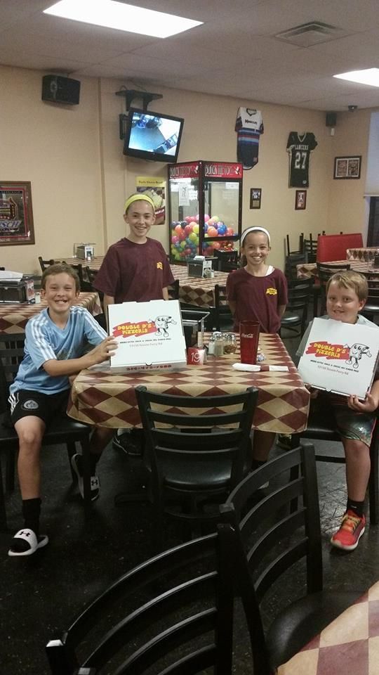 Four children hold certificates at a table in a restaurant, smiling toward the camera.