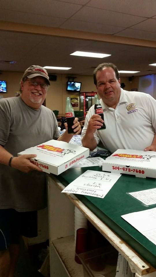 Two men at a counter holding pizza boxes in a casual indoor gathering