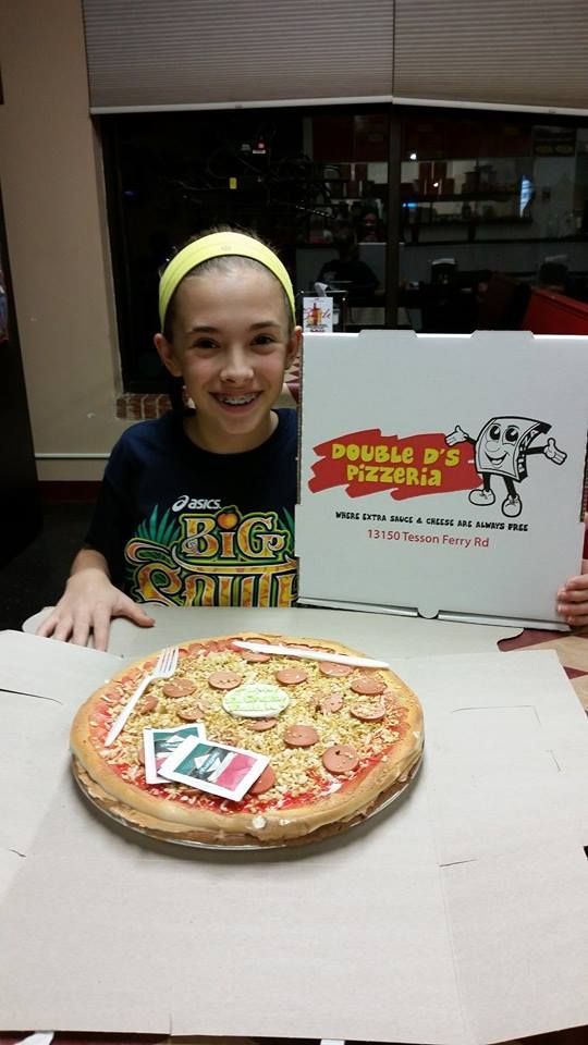 Person smiling at a table with a pizza and a Domino's Pizza box, indoors.