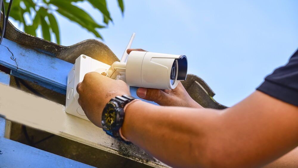 A man is installing a white home security camera on the roof of a house — Short Stop Electrical in Nerang, QLD