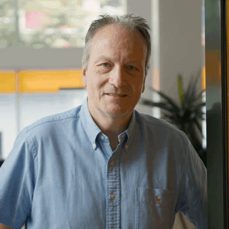 Un homme en chemise bleue se tient devant une fenêtre